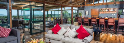 Ein einladender Lounge-Bereich mit gemütlichem Sofa, bunten Kissen und Blick auf die umliegende Natur durch große Fenster.