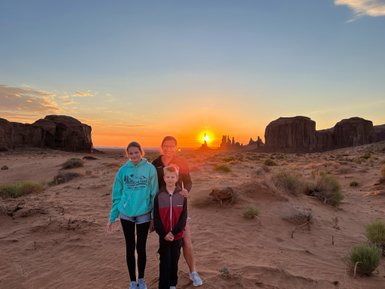 Drei Personen stehen im Monument Valley, während die Sonne hinter den Felsen untergeht und den Himmel in warmen Farben erleuchtet.