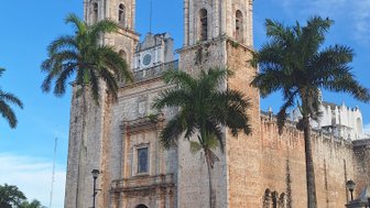 Die beeindruckende Kirche mit zwei Türmen steht vor einem strahlend blauen Himmel, umgeben von Palmen und historischen Gebäuden.