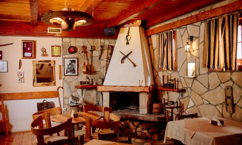 Ein rustikales Restaurant mit Holzmöbeln, einem offenen Kamin und dekorativen Werkzeugen an den Wänden.
