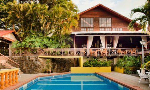 Ein einladender Poolbereich umgeben von üppigem Grün und einem charmanten Holzhaus im Hintergrund, ideal für Familienurlaube.