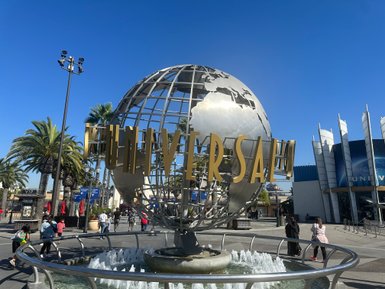 Die goldene Universal-Kugel steht im Vordergrund, umgeben von Palmen und Besuchern, die den Freizeitpark betreten.