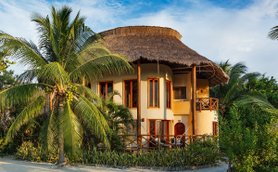 Ein charmantes Hotel mit einem strohgedeckten Dach, umgeben von üppigen Palmen und tropischer Vegetation.