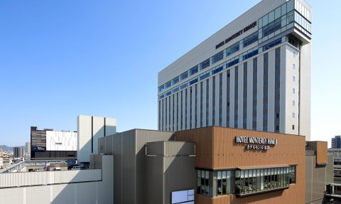 Das moderne Hotel Monterey Himeji präsentiert sich mit einer eleganten Fassade und klaren Linien unter einem strahlend blauen Himmel.