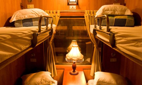 Ein gemütlicher Schlafwagen mit zwei Etagenbetten, einem Tisch und einer warmen Lampe, die eine einladende Atmosphäre schafft.
