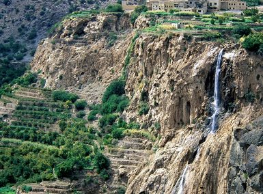 Aussicht auf die Felslandschaft des Jebel Akhdar mit einem kleinen Wasserfall inmitten der grünen Täler – Oman Reise mit Kindern