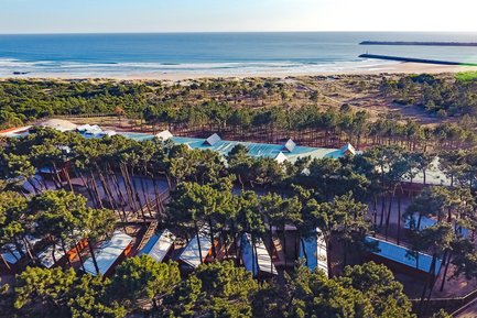Eine Luftaufnahme zeigt ein Hotel inmitten von hohen Bäumen, umgeben von einem schönen Strand und dem Ozean im Hintergrund.