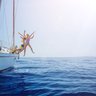 Drei Kinder springen fröhlich von einer Yacht ins glitzernde blaue Wasser, umgeben von einem klaren Himmel.
