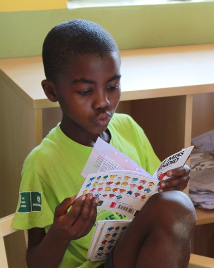 Ein Junge sitzt auf einem Stuhl und liest konzentriert in einem bunten Buch, während er seine Beine anzieht.