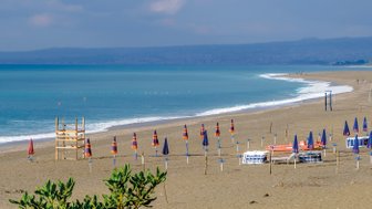 Ein ruhiger Strand mit blauen und orangefarbenen Sonnenschirmen, die auf dem goldenen Sand aufgestellt sind.