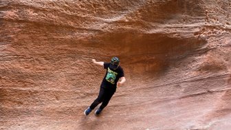 Ein Kind springt fröhlich über eine glatte, rotbraune Felsoberfläche in einer beeindruckenden Schlucht.