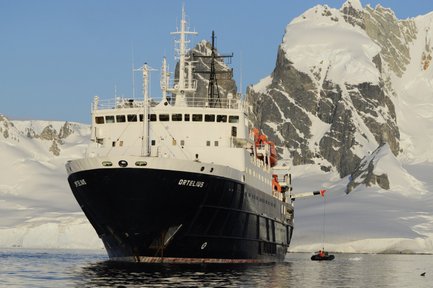 Das Forschungsschiff Ortelius liegt vor schneebedeckten Bergen in der Antarktis, während ein kleines Boot ablegt.