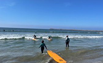 Surfer in einem Neoprenanzug geht ins Wasser, während andere auf ihren Surfbrettern warten, um die Wellen zu reiten.