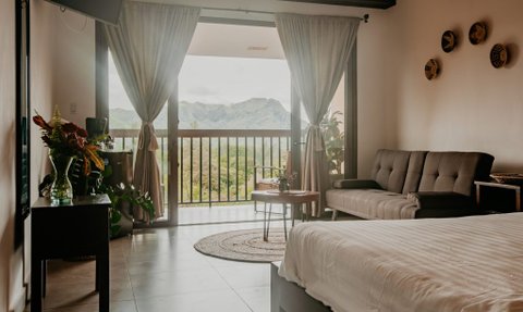 Ein gemütliches Zimmer mit einem grauen Sofa, einem kleinen Tisch und Blick auf die Berge durch große Fenster.