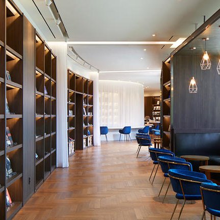 Ein moderner Lesebereich mit eleganten Bücherregalen und gemütlichen blauen Stühlen, ideal für entspannte Stunden.