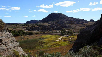 Eine weite Landschaft mit sanften Hügeln und einem markanten Berg im Hintergrund, unter einem strahlend blauen Himmel.