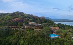Ein modernes Hotelgebäude schmiegt sich an einen bewaldeten Hang, umgeben von üppigem Grün und sanften Hügeln.