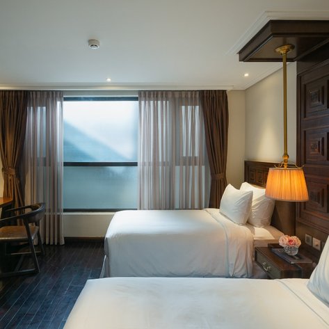 Ein elegantes Hotelzimmer mit zwei Betten, einem Schreibtisch und großen Fenstern, die sanftes Licht hereinlassen.