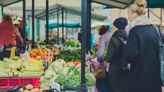 Ein belebter Markt mit frischem Gemüse und Obst, wo Menschen in bunten Ständen stöbern und einkaufen.