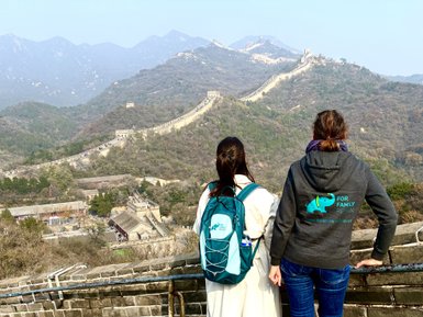 Zwei Frauen stehen auf der Chinesischen Mauer und blicken auf die beeindruckende Landschaft der Berge und Wälder.