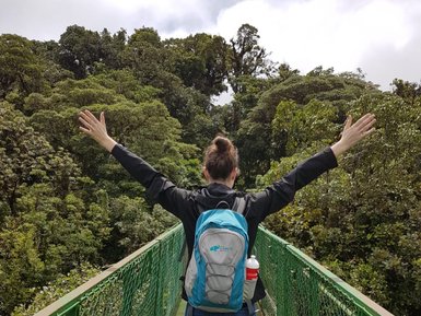 Eine Frau überquert eine Hängebrücke hoch über dem Boden im tropischen Regenwald – Costa Rica Reise mit Kindern