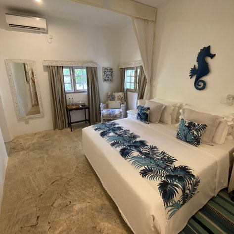 Ein helles Zimmer mit einem großen Bett, dekoriert mit blauen Palmenmustern und einem eleganten, minimalistischen Stil.