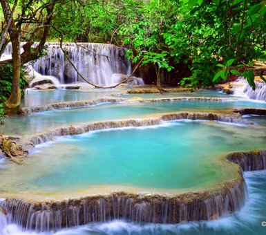 Die Kuang Si Wasserfälle zeigen mehrere kaskadierende Wasserfälle, die in türkisfarbenen Becken landen, umgeben von üppigem Grün.