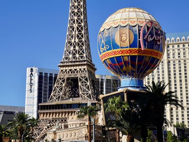 Der Eiffelturm in Las Vegas erhebt sich majestätisch über die bunten Gebäude und Palmen der Stadt unter strahlend blauem Himmel.