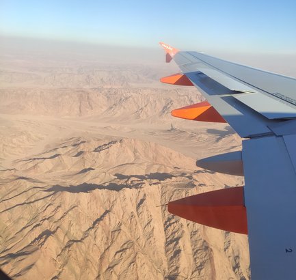 Der Blick aus dem Flugzeug zeigt die schroffen, braunen Berge und das klare, blaue Himmel über einer weiten Wüstenlandschaft.