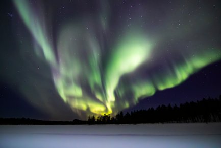 Ein atemberaubendes Nordlicht erhellt den Nachthimmel über einer verschneiten Landschaft in Finnland.