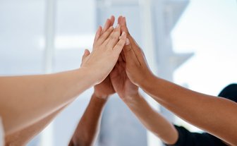Fünf Hände verschiedener Hauttöne berühren sich in einem positiven Moment des Zusammenhalts und der Zusammenarbeit.