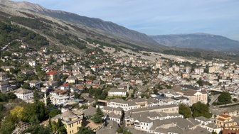 Ein weitläufiger Blick auf die Stadt Gjirokaster, umgeben von sanften Hügeln und majestätischen Bergen im Hintergrund.
