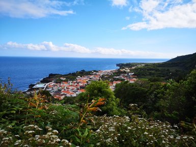Ein malerischer Blick auf ein Küstendorf mit roten Dächern, umgeben von üppigem Grün und dem blauen Ozean im Hintergrund.