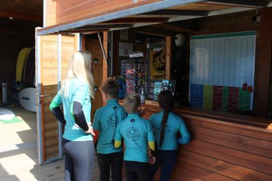 Eine Gruppe von Kindern und einem Erwachsenen steht an einem Kiosk, um sich über Wassersportaktivitäten zu informieren.