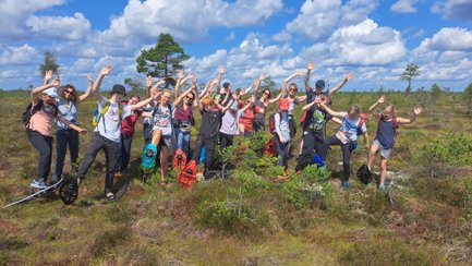 Eine Gruppe von Menschen mit Schneeschuhen posiert fröhlich in einer Moorlandschaft unter einem blauen Himmel mit Wolken.