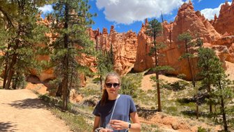 Eine junge Frau steht auf einem Wanderweg im Bryce Canyon, umgeben von beeindruckenden roten Felsformationen und grünen Bäumen.