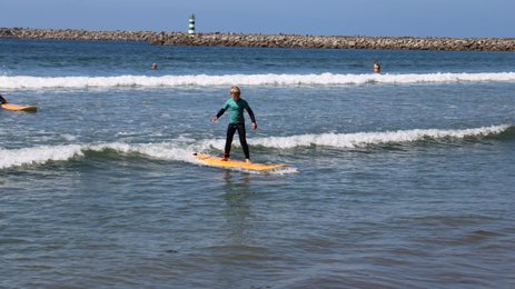 Ein junger Surfer balanciert auf einem orangefarbenen Brett und reitet eine Welle im klaren Wasser des Strandes.
