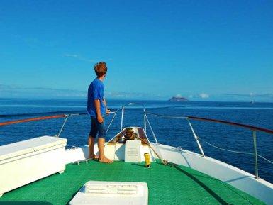 Ein Junge steht auf dem Deck eines Bootes und blickt auf das ruhige Wasser und eine entfernte Insel im Hintergrund.