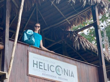 Eine Frau steht auf einem Balkon des Heliconia Amazon River Lodge in Peru, lächelnd mit einem Rucksack auf der Schulter.
