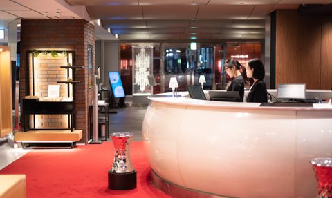 Die Empfangstheke eines modernen Hotels mit zwei Mitarbeiterinnen, die an Computern arbeiten, umgeben von stilvollem Interieur.