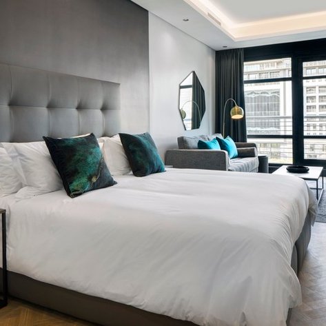 Ein modernes Schlafzimmer mit einem großen Bett, eleganten Kissen und einem gemütlichen Sitzbereich neben einem Fenster.