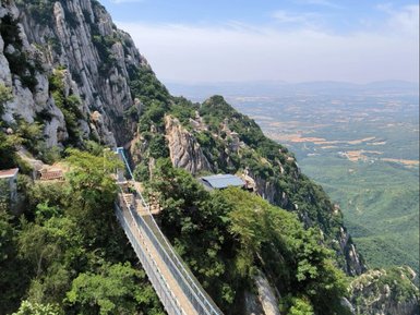 Eine schmale Hängebrücke führt über eine steile Klippe, umgeben von üppigem Grün und beeindruckenden Felsformationen.