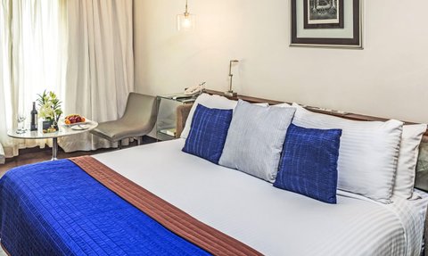 Ein stilvolles Schlafzimmer mit einem großen Bett, blauen Kissen und einem eleganten Tisch mit Obst und Wein.