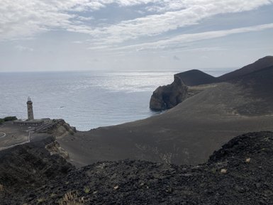 Ein Leuchtturm steht majestätisch an der Küste, umgeben von schwarzem Vulkangestein und dem glitzernden Ozean.