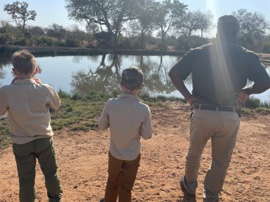 Kinder stehen mit Safari-Guide vor einem Wasserloch im Krüger Nationalpark – Südafrika Familienreise