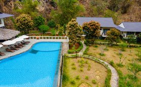 Ein atemberaubender Blick auf einen blauen Pool, umgeben von üppigem Grün und modernen Bungalows in einer ruhigen Berglandschaft.