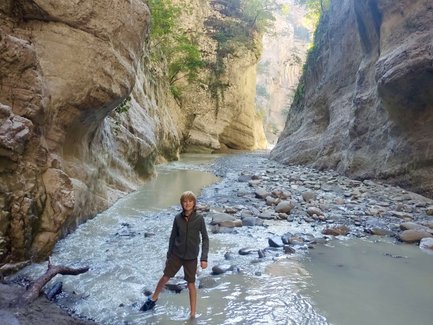 Ein Junge steht im flachen Wasser eines Canyons, umgeben von hohen, steilen Felswänden und üppigem Grün.