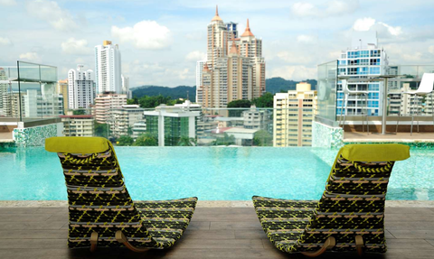 Zwei Liegestühle mit buntem Muster stehen am Rand eines Infinity-Pools mit Blick auf eine Stadtlandschaft.
