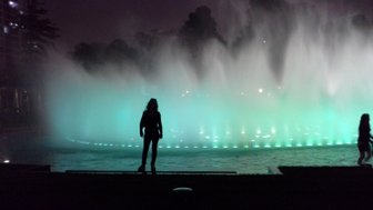 Eine Silhouette einer Person steht vor einem beleuchteten Wasserfall, der in sanften Grüntönen leuchtet.