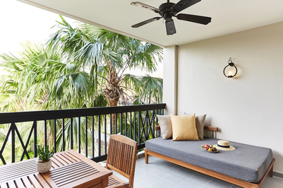 Ein einladender Balkon mit einem grauen Sofa, einem Tisch und üppigen Palmen im Hintergrund, ideal für Entspannung.